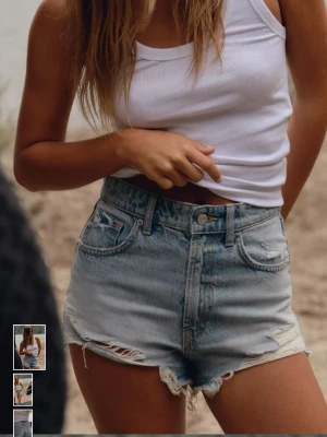 Högmidjade ljusblå jeansshorts - Säljer ett par högmidjade ljusblå jeansshorts med slitna detaljer och råa kanter. Shortsen har klassisk femficksdesign och dragkedja med knapp. Perfekta för varma dagar och ger en avslappnad vibe. Aldrig använda o lappar kvar! 