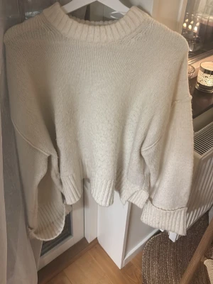 Vit  stickad tröja Gina Tricot - Säljer en vit  stickad tröja från Gina Tricot i storlek S. Tröjan har bred ribbad kant vid hals, ärmslut och nederkant samt en loose passform med långa ärmar. Perfekt för lager på lager under höst och vinter.