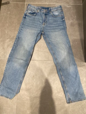 Blå tapered jeans från H&M, strl 158 - Säljer ett par ljusblå jeans från H&M i storlek 158. Modellen har relaxed fit, justerbar midja och avsmalnande ben. Klassisk femficksdesign och snygga kontrastsömmar. Perfekta till vardags för en avslappnad look.