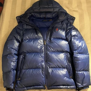 Blå dunjacka Polo Ralph Lauren XS - Snygg blå dunjacka från Polo Ralph Lauren i storlek XS, men sitter mer som S. Jackan har en pufferstil med huva, flera dragkedjefickor och klassisk logga broderad på bröstet. Perfekt för kalla dagar med sin quiltade design och stilrena look. Användes under 1 vinter så lite skavanker finns men inget märkvärdigt! Hör av dig vid minsta lilla!🤩🤗