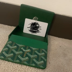 G plånbok grön - Snygg grön plånbok från G med det klassiska grafiska mönstret i vitt och brunt. Plånboken har flera kortfack och kommer i original ask. Perfekt för dig som vill ha något unikt och lyxigt i fickan. Plånboken e aldrig andvänd. Nytt skick.