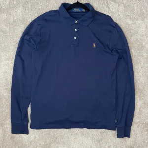 Ralph Lauren pikétröja - Säljer en snygg mörkblå pikétröja från Ralph Lauren i slim fit. Tröjan har långa ärmar och den klassiska broderade loggan på bröstet. Perfekt för både vardag och lite finare tillfällen. Materialet är mjukt och bekvämt. Passar perfekt till höst och vår! 