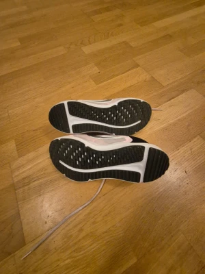 Nike rosa sneakers med snörning - Säljer ett par snygga Nike sneakers i ljusrosa med vita detaljer och svart häl. Skorna har en rund tå, platt sula och är tillverkade i syntetmaterial med mesh-överdel för bra ventilation. Klassisk Nike-logga på sidan och snörning framtill.