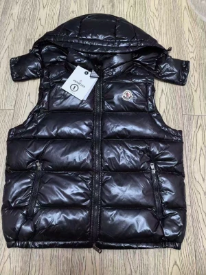 Svart dunväst från Moncler med huva - Svart, glansig dunväst från Moncler med avtagbar huva och två dragkedjeförsedda fickor framtill. Västen har ett quiltat mönster och Moncler-logga på bröstet. Perfekt för lager-på-lager och har en clean, modern look.