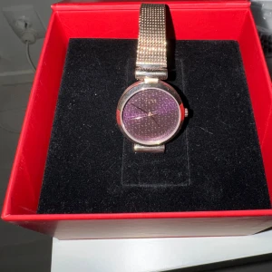 Hugo Boss damklocka meshlänk  - Snygg klocka från Hugo med lila urtavla och diskret mönster. Armbandet är i roseguldigt metallnät som ger en modern vibe. Rund boett och minimalistisk design, perfekt för dig som gillar stilrena accessoarer med lite edge.