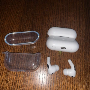 AirPods Pro - Snygga Apple AirPods Pro med laddningsetui, skyddsfodral och laddkabel. Hörlurarna är i gott skick utan synligt slitage och fungerar utmärkt. Perfekt för trådlös musik och samtal med aktiv brusreducering. Komplett med tillbehör för extra skydd och bekvämlighet.