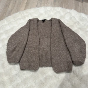 Beige stickad kofta från Lindex - Mysig beige stickad kofta från Lindex i storlek XS/S. Koftan har långärmade, lite loose ärmar och är öppen framtill utan knappar. Perfekt att slänga på sig när det är kyligt ute. Materialet är mjukt och ger en chill vibe.