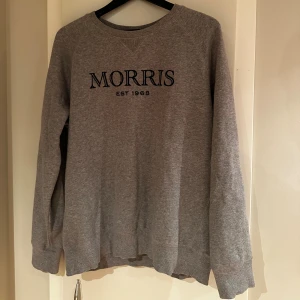 Grå sweatshirt från Morris, L - Snygg grå sweatshirt från Morris med svart broderad logga och text 'EST 1968' på bröstet. Tröjan har rund hals, långa ärmar och ribbade muddar. Perfekt för chill dagar och enkel att matcha med jeans eller joggers.