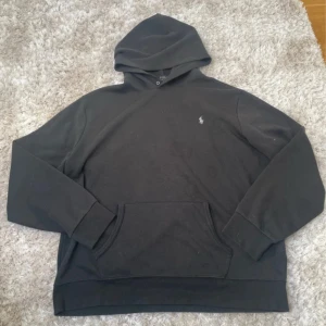 Svart hoodie från Polo Ralph Lauren XXL - Svart hoodie från Polo Ralph Lauren i storlek XXL. Klassisk design med huva, känguruficka och diskret logga broderad på bröstet. Tröjan har långa ärmar och är tillverkad i mjuk bomull, perfekt för chill dagar. Snygg och enkel att matcha med jeans eller joggers. Har ett par fläckar på framsidan