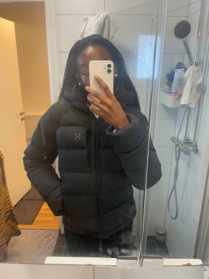 Svart pufferjacka från Haglöfs - Säljer en svart pufferjacka från Haglöfs i modellen Rosson Down Hood W True Black i storleken S med huva och dragkedja framtill. Jackan har en clean look med diskret logga på bröstet och är perfekt för kalla dagar. Den är långärmad och har en oversized passform som ger en chill vibe.