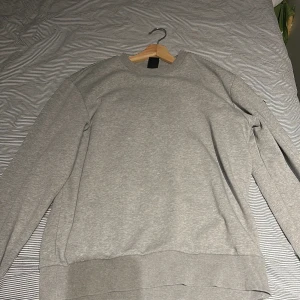 Grå sweatshirt från Colmar Originals - Snygg grå sweatshirt från Colmar Originals med rundad hals och ribbade muddar vid ärmslut och nederkant. Tröjan har lång ärm och en diskret Colmar-logga på ena ärmen. Perfekt för chill dagar och enkel att matcha med jeans eller joggers. Pris kan diskuteras vid snabb affär, för att den har en liten missfärgning på ena armen.