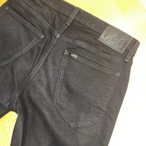 Svarta jeans från Lee (29/32) - Svarta jeans från Lee med klassisk femficksdesign och Lee-logga på bakfickan. Jeansen har smal passform och raka ben, tillverkade i stretchig bomullsdenim för en bekväm känsla. Perfekta för dig som gillar en clean och stilren look. ”Daren Zip Fly” i storlek W29 L32.
