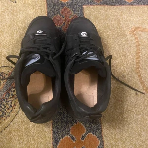 Buffalo London svarta sneakers - Buffalo London sneakers i helsvart med rund tå och platt sula. Skorna har snörning och är tillverkade i skinn med textilfoder. Klassisk chunky stil med Buffalo-logga på plösen och framtill. Perfekta för dig som gillar retrovibbar och streetwear.