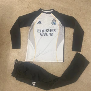 Real Madrid långärmad fotbollströja Adidas - Säljer en långärmad Real Madrid fotbollströja från Adidas i vitt och svart med gula detaljer. Tröjan har klubbmärke och sponsortryck på bröstet samt dragkedja vid halsen. Materialet är lätt och andas, perfekt för träning eller match.