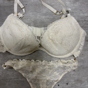 Champagnefärgad spetskorsett med glitter - Säljer en champagnefärgad korsett med matchande spetsdetaljer och glittriga inslag. Toppen har justerbara axelband med små rosetter och guldfärgade ringar. Spetsen är broderad och ger en lyxig känsla, perfekt för dig som gillar eleganta underkläder.