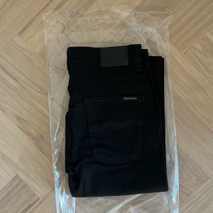 Helt nya Nudie Jeans -  Slim Jim - W32 L32 - Helt nya och oanvända Nudie Jeans Co Slim Jim i färgen Dry Black – fortfarande i originalförpackning (se bilder).  En tidlös och elegant modell i helsvart rådenim med perfekt balans mellan klassisk passform och modern stil.  Detaljer: • Modell: Slim Jim • Storlek: W32 / L32 • Färg: Dry Black (matt svart rådenim) • Passform: Regular slim – normal midja, lätt avsmalnande ben • Material: 99% ekologisk bomull, 1% elastan • Tillverkade i Italien • Varumärke: Nudie Jeans Co (Göteborg)