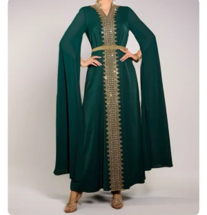 Grön långklänning med gulddetaljer - Elegant grön långklänning med v-ringning och breda, svepande ärmar. Klänningen har dekorativa guldfärgade broderier längs hela framsidan och ett matchande bälte i midjan. Perfekt för dig som vill sticka ut med stilrena detaljer och lyxig känsla.