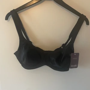 Svart bikiniöverdel från Trofé 75C - Snygg svart bikiniöverdel från Trofé i storlek 75C. Klassisk modell med breda axelband och slät yta, perfekt för dig som vill ha en stilren look på stranden eller vid poolen. Materialet känns mjukt och bekvämt mot huden.