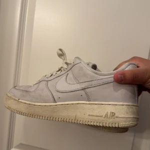 Nike Air Force 1 vita mockasneakers - Säljer ett par klassiska Nike Air Force 1 sneakers i vitt mocka. Skorna har en låg siluett, snörning och den ikoniska Air-sulan. Perfekta för dig som gillar en clean och tidlös look. Swoosh-loggan på sidan och perforerade detaljer på tån.