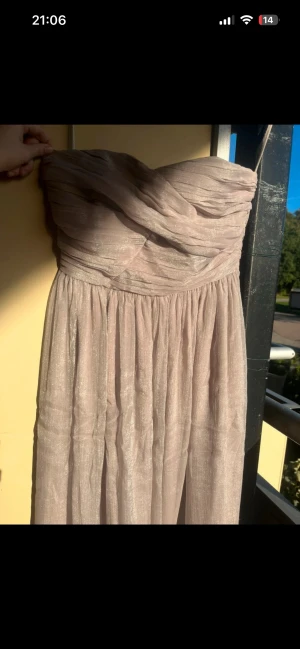 Grå långklänning Selected Femme - Säljer en elegant axelbandslös långklänning från Selected Femme i skimrande grå. Klänningen har draperad överdel och ett lätt, glansigt tyg som faller snyggt. Perfekt för dig som vill ha en stilren och sofistikerad look.passar M eller liten L