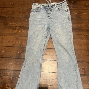 Bootcut jeans med snörning i midjan - Snygga ljusblå bootcut jeans med unik snörning i midjan istället för dragkedja. Klassisk femficksmodell och mjukt denimtyg som ger en chill vibe. Perfekta för dig som vill sticka ut med detaljer och gillar retrostil.