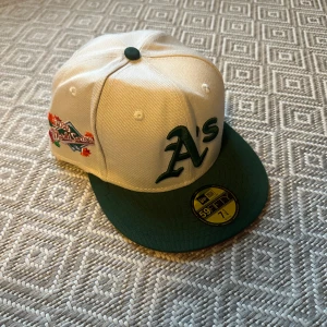 Oakland A's 59FIFTY keps från New Era - Snygg Oakland Athletics 59FIFTY keps från New Era, vit med grön skärm och broderad A's-logga framtill. World Series-patch på sidan och röd underskärm. Perfekt för dig som gillar baseball och streetwear. Kepsen är använd max 5 gånger och har sedan i somras bara legat i en låda vilket föklarar att kepsen är lite fel formad. Kan enkelt fixa det om det är ett behov