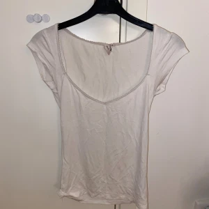 Vit topp med spetskant från Nelly XS - Söt vit topp från Nelly i storlek XS. Modellen har korta ärmar, v-ringad halsringning och en fin spetskant runt halsen. Tillverkad i mjuk bomull, perfekt för en enkel och clean look.