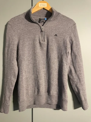 Grå half zip polotröja J.Lindeberg - Snygg grå polotröja från J.Lindeberg med half zip. Tröjan är stickad i mjuk ull och har ribbade muddar vid hals, ärmslut och nederkant. Från början i storlek L men krympt i tvätten så är nu xs/s snarare. 
