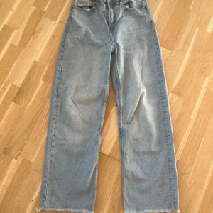 Ljusblå jeansbyxor från 157, XS - Säljer ett par ljusblå jeansbyxor från 157 i storlek XS. Modellen har raka ben med rå kant nedtill och klassisk femficksdesign. Jeansen är tillverkade i bomull och har en avslappnad, loose passform som ger en cool vibe.