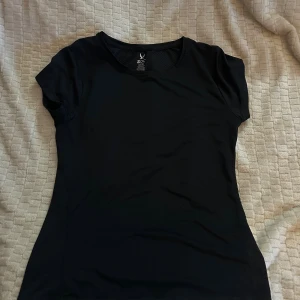 Svart träningstopp från SOC - Svart, kortärmad träningstopp från SOC med rund hals. Toppen är slim fit och tillverkad i ett syntetmaterial som andas, perfekt för gymmet eller löprundan. Enkel och stilren design som passar till alla träningsoutfits.