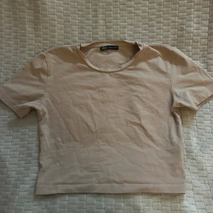 Beige croppad t-shirt från Zara - Säljer en enkel och stilren beige t-shirt från Zara. Modellen är croppad med rund hals och korta ärmar. Materialet är mjuk bomull som känns skönt mot huden. Perfekt för dig som gillar minimalistisk stil och neutrala färger.