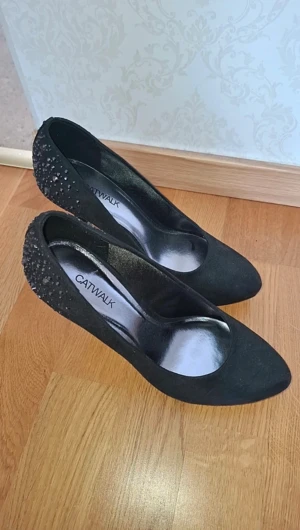 Svarta pumps med strass från Catwalk - Snygga svarta pumps från Catwalk med spetsig tå och hög klack. Baksidan är dekorerad med glittrande setnar som ger extra edge. Skorna är gjorda i mocka-look och har en elegant siluett som lyfter din outfit. Använt enbart inomhus