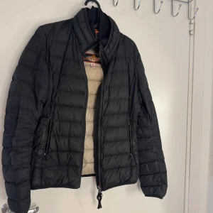 Svart dunjacka Parajumpers XS - Svart dunjacka från Parajumpers i storlek XS. Jackan är quiltad med beige insida, har hög krage och två dragkedjefickor fram. Märkespatch på ärmen och coolt Super Lightweight-tryck på insidan. Perfekt för dig som vill ha en lätt och snygg jacka.