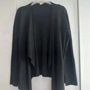 Svart omlottkofta med långa ärmar - Svart kofta från H&M med omlott-design och långa ärmar. Koftan har en avslappnad passform och perfekt att slänga på sig när det är lite kyligt. Den har ett snyggt fall framtill och är enkel att matcha med olika outfits