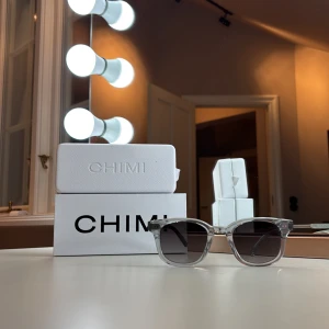 CHIMI transparenta solglasögon - Snygga solglasögon från CHIMI med transparent båge och rektangulär form. Glasen är mörktonade och ger en cool kontrast mot den klara bågen. Perfekt accessoar för dig som gillar stilrena detaljer och modern design.