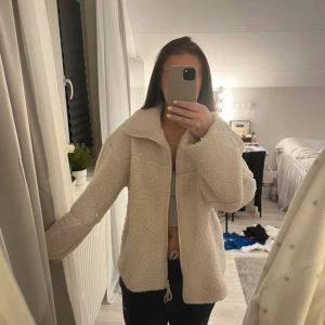 Beige teddyjacka med dragkedja - Säljer en fluffig och oversized teddyjacka i beige med hel dragkedja framtill och hög krage. Jackan har långärmade ärmar och är perfekt för dig som gillar mysiga och trendiga plagg. Passar dig som vill ha en chill och cool stil. 