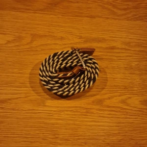 Randigt flätat bälte med läderdetaljer - Snyggt flätat bälte med svart och vitt zigzag-mönster. Bältet har bruna läderdetaljer vid spännet och ändarna samt ett silvrigt metallspänne. Perfekt accessoar för att lyfta din outfit med en cool och modern touch.