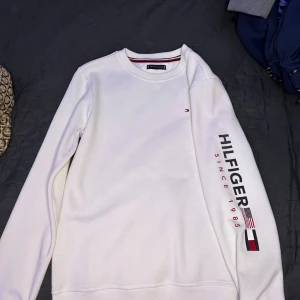 Sällsynt Tommy Hilfiger Sweatshirt - Vit sweatshirt från Tommy Hilfiger med tryck på vänstra ärmen, Limitiserad och väldigt sällsynt att få tag I, Storlek Small, Köpt runt 2020 och använt ett fåtal gånger så skicket är felfritt. Öppen att diskutera priset, kontakta mig vid fler frågor!