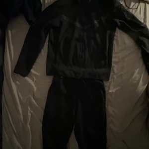 Svarta Nike mjukisbyxor med snörning - Svarta mjukisbyxor från Nike med klassisk logga på benet och snygg snörning i midjan. Byxorna har en loose passform och är gjorda i mjukt bomullsmaterial, perfekta för chill eller träning. Snyggt och enkelt streetwear-plagg för dig som gillar sportig stil.