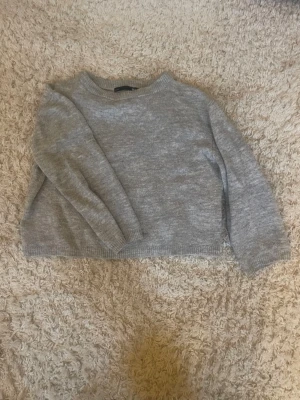 Grå stickad tröja i loose fit - Mysig grå stickad tröja med rund hals och avslappnad passform. Tröjan har långa ärmar och ribbade muddar vid hals, ärmslut och nederkant. Perfekt för lager på lager under kyliga dagar. Använd ett fåtal gånger. Säljer då den blev för liten