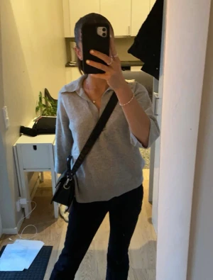 Grå stickad polotröja med v-ringning - Säljer en grå stickad polotröja med v-ringad hals och krage. Tröjan har trekvartsärm och en relaxed, loose passform som ger en chill vibe. Perfekt att slänga på sig till jeans eller leggings för en enkel men snygg look.