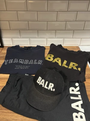 Svart och mörkblå BALR. t-shirt - Kläder från BALR! Två T-shirts, ett par shorts och en keps. Allt är i bra skick förutom kepsen som är lite sliten i spänet!! Hör av er vid mer frågor😁