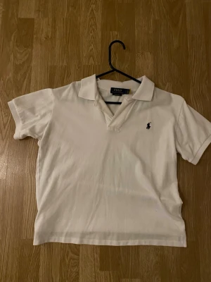 Vit pikétröja från Polo Ralph Lauren - Klassisk vit pikétröja från Polo Ralph Lauren i modellen Custom Slim Fit. Tröjan har korta ärmar, krage och knappslå samt den ikoniska broderade loggan på bröstet. Tillverkad i mjuk bomull som känns skön mot huden.