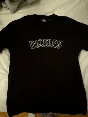 Svart Dickies t-shirt med tryck - Svart t-shirt från Dickies i bomull med stort vitt tryck på bröstet. Dickies-logga även längst ner. Tröjan är det kraftigare/tjockare slaget!