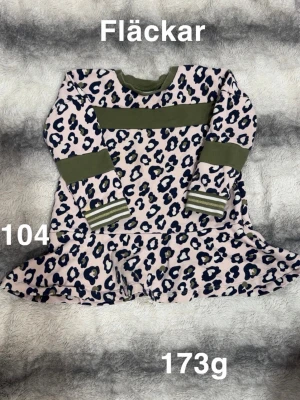 Leopardmönstrad klänning i rosa och grön - Säljer en söt leopardmönstrad klänning i ljusrosa. Klänningen har långärmade ärmar, gröna ribbade muddar och en bred grön rand över bröstet. Kjolen är utställd. 🌸 Fläckar. Storlek 104.