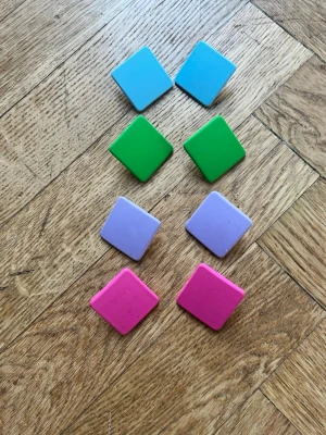 Färgglada fyrkantiga örhängen - Säljer ett set med fyra par stora fyrkantiga örhängen i plast, ca 3,5 cm breda. Färgerna är blå, grön, lila och rosa. Perfekta för dig som vill sticka ut och addera färg till din look. Alla har stift och plastpluppar på baksidan.