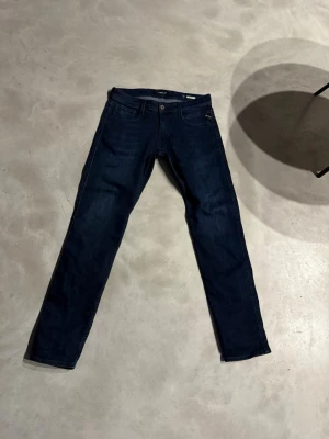 Replay Anbass mörkblå jeans - Säljer ett par mörkblå Replay Anbass jeans med klassisk femficksdesign och snygga detaljer vid fickorna. Jeansen har en rak passform och är tillverkade i mjukt denimtyg som sitter skönt hela dagen. Perfekta till sneakers eller boots.