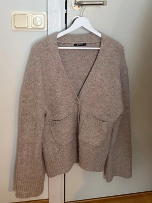 Beige stickad kofta från Gina Tricot - En beige stickad kofta från Gina Tricot med v-ringning, stora framfickor och en knappar framtill. 