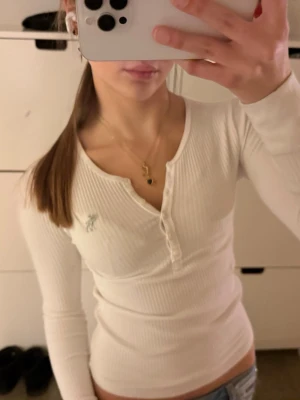 Henley farfarströja långärmad Abercrombie & fitch  - Henley Abercrombie & Fitch långärmad topp i vitt. Barnstorlek 11/12 men passar en vanlig XS. Mycket bra skick! En rad funktionella knappar, du kan öppna eller stänga dem för att justera stilen. Klassisk Abercrombie & Fitch älglogotyp i silver broderad på bröstet. Följ för fler liknande kläder och köp paket!