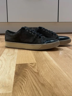  Lanvin (prisförslag) - Säljer ett par svarta sneakers från Lanvin med ovandel i mocka och lackad tå. Skorna har svarta snören, rund tå och beige sula. Klassisk och stilren modell som passar till mycket. Märket syns på sulan undertil. Skriv vid minsta lilla!